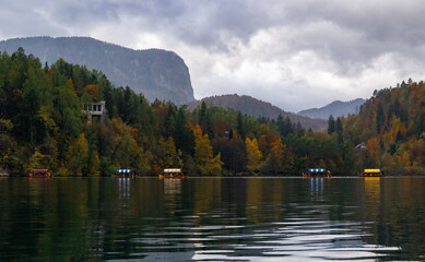 Scenic autumn view of Lake Bled in Slovenia with colorful boats on water and forested mountain background