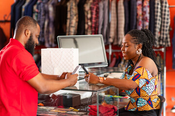 Mobile money, cashless digital payment, African businesswoman processes a successful transaction for a customer in her fashion clothing boutique