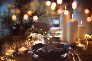 Elegant table decoration for a christmas dinner. Romantic dinner concept with burning candles in the evening at a restaurant. Close-up with golden bokeh lights. Background for seasonal an holiday gast