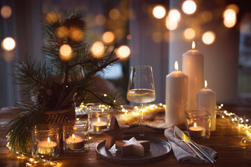 Elegant table decoration for a christmas dinner. Romantic dinner concept with burning candles in the evening at a restaurant. Close-up with golden bokeh lights. Background for seasonal an holiday gast