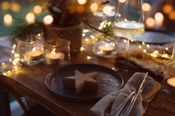 Elegant table decoration for a christmas dinner. Romantic dinner concept with burning candles in the evening at a restaurant. Close-up with golden bokeh lights. Background for seasonal an holiday gast