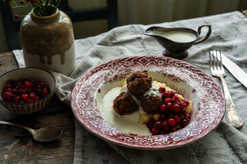Traditional Swedish meatballs with mashed potatoes, cranberries and creamy gravy in vintage plate on wooden table. Homemade dinner. Comfort food.