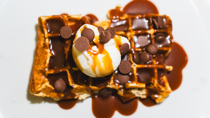 Crispy waffle topped with vanilla ice cream, chocolate sauce, caramel, and fresh fruits. A decadent dessert ready to eat, perfect for indulgent treats and cafes.