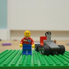Naklejka premium Lego minifigure stands next to a small race car on a green baseplate