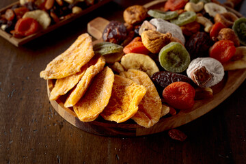 Dried mango slices, tropical fruits, nuts, and raisins on a wooden table.