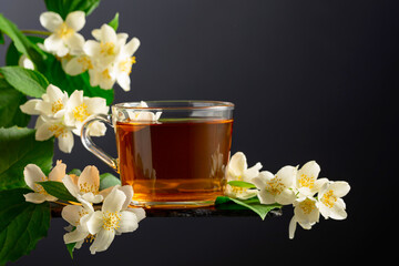 Cup of jasmine tea and fresh jasmine flowers on a black background.