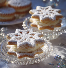 Weihnachtliche Plätzchen in Sternform mit Cremefüllung und Puderzucker auf Glasgeschirr