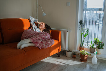 Young pregnant woman with toxicosis resting on a sofa under a blanket, looking unwell and fatigued...