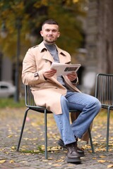Fototapeta premium Young man reading newspaper on chair outdoors