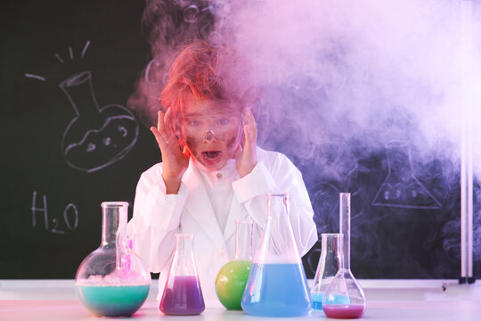 Back to school. Boy doing chemical research at desk against chalkboard with formulas indoors