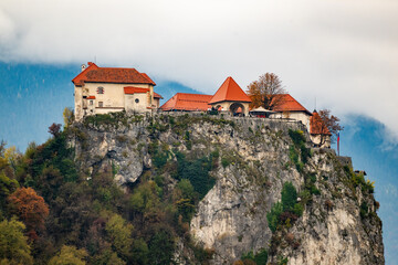 castle on rocky hilltop surrounded by autumn foliage with cloudy sky at lake bled slovenia