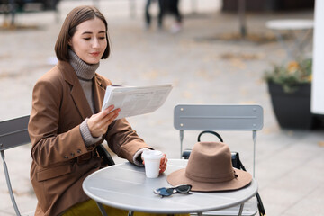 Elegant woman in suit reading newspaper in outdoor cafe