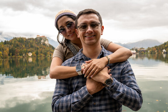 Young couple celebrating engagement by Lake Bled with autumn forest and mountains in Slovenia