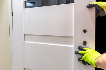 Installation of a black door handle with a lock for a white wooden door,