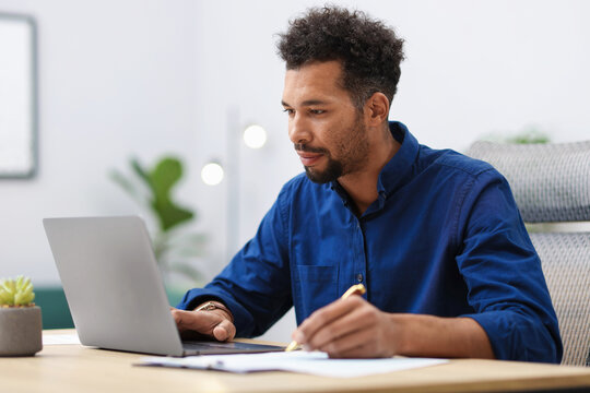 Man working with laptop and writing at table in office