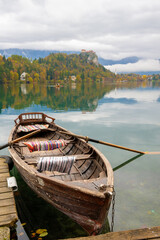 wooden boat docked on lake bled with autumn foliage and castle on hill in slovenia
