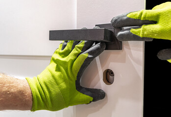 Installation of a black door handle with a lock for a white wooden door,