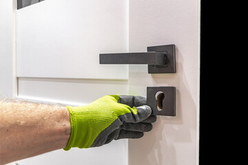 Installation of a black door handle with a lock for a white wooden door,
