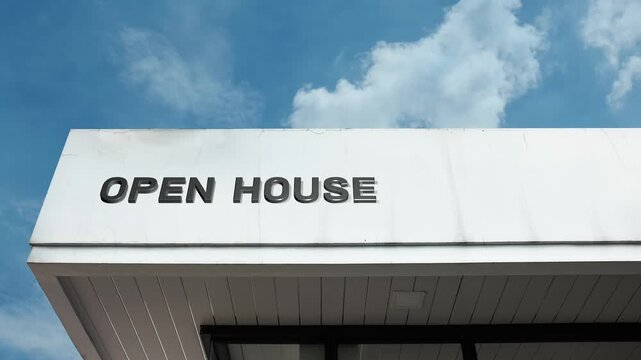 An open house word sign displayed on a residential or commercial building under a clear blue sky, symbolizing real estate viewing, property sales, and public access events