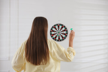 Woman with dart aiming at dartboard indoors, back view