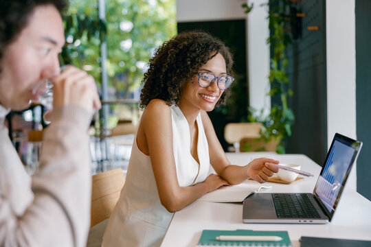 woman diligently working on laptop while exchanging smiles with colleague in stylish cafe