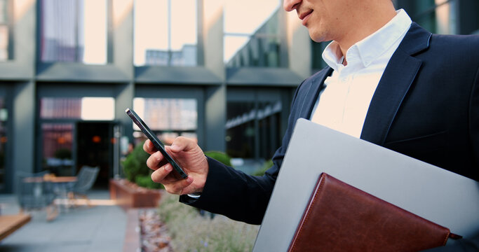 Male hands holding smartphone and laptop walking at downtown area. Businessman, hands and typing with phone in city for communication, social media or outdoor. - Powered by Adobe
