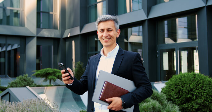 Portrait of elegant caucasian businessman is using his smartphone after he smiles into the camera.