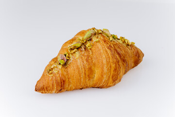 Golden croissant topped with chopped pistachios on white background, gourmet bakery dessert