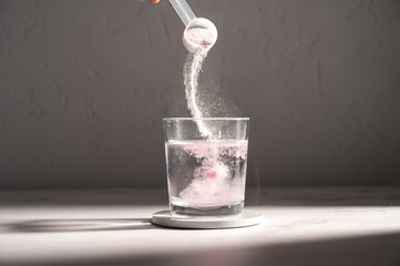Pouring food supplement powder in glass of water. Collagen, protein powder, vitamins.