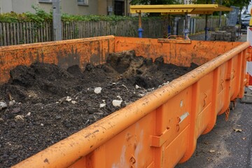 Large orange container filled with soil and gravel at a construction site.