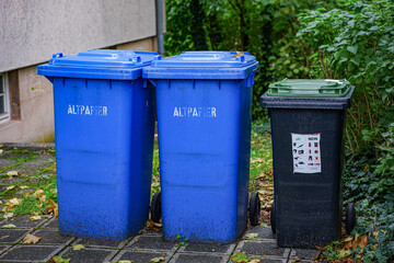 Recycling bins in the yard: two blue paper containers and one black bin for general waste.