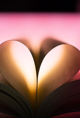 Book pages folded into a heart under gentle pink lighting. Romantic and poetic concept symbolizing love for reading, literature, storytelling and imagination.