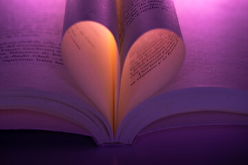 Romantic heart shape made with book pages under purple and warm light. Symbolic image of love for reading, imagination, storytelling and poetic literature.