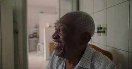 Elderly man of African descent laughing joyfully in tiled kitchen, expressing happiness and connection, candid everyday moment in a warm home setting