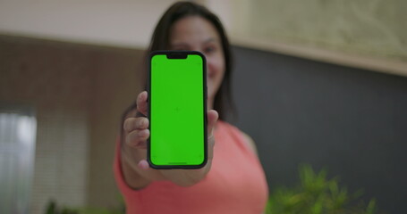 Woman extending smartphone with green screen and chroma key towards the viewer, emphasizing customizable screen, vibrant outdoor setting with blurred focus in the background