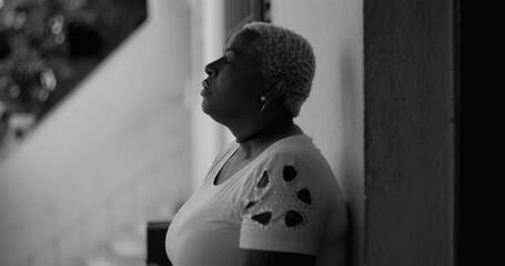 African American woman leaning against a wall, gesturing with hand, expressing despair and introspection in a monochromatic setting, themes of regret and sorrow