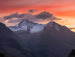 Dramatic sunset paints the sky with vibrant orange and pink hues over snow capped mountains