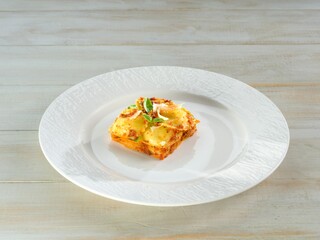 A single, perfectly portioned piece of lasagna sits on a white plate, garnished with basil. Ready to eat, it shows its rich, layered texture