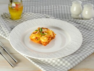A single serving of pasta is presented on a white plate, with a small carafe of beverage and seasoning shakers. Cutlery is placed at the left side of the plate, ready for service