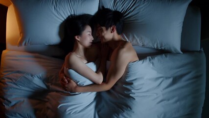 couple cuddling in bed at night, embracing under soft blue bedding, peaceful sleep with warm bedside glow, intimacy and affection, top‑down overhead view in a cozy bedroom with pillows - Powered by Adobe