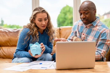 Two people discuss finances while reviewing documents and using a laptop at home in bright natural light during the day