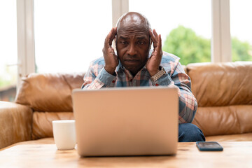 Senior man feeling stressed while working on laptop in bright living room