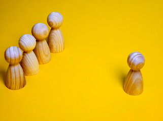 Wooden figure standing apart from the crowd on a yellow background