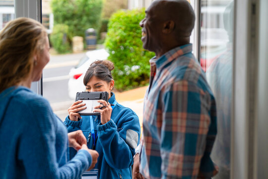 Friends gather at home for a fun moment while recording happy memories on a tablet in the afternoon light