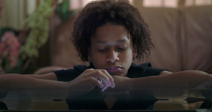 Close-up of boy leaning on arms staring at smartphone, vacant expression, glass table reflection, highlighting emotional apathy and detachment from surroundings