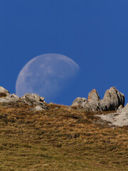Luna diurna asomando sobre ladera alpina y rocas bajo cielo azul, Andorra, Pirineos, Europa