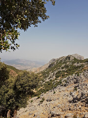 Ridgelines and rugged cliffs rise to reveal cliffs and hills far below in a sunlit landscape.