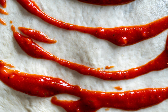 Tomato sauce for pizza on dough. The process of making pizza. Close-up, top view