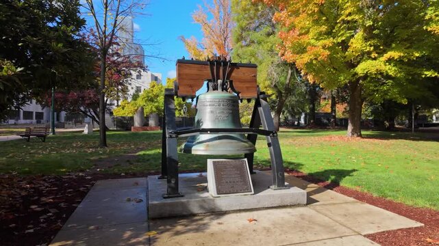 A clear view of the Liberty Bell replica displayed on the grounds of the Oregon State Capitol in Salem, with the distinctive white marble and gold-domed capitol building visible in the background.