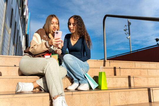 Gen z friends shopping using smartphone on stairs